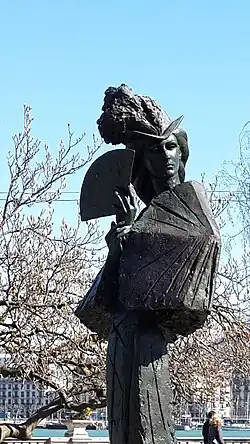 Photo en couleurs d'un buste sur un pilier représentant une femme sculptée portant un chapeau à plumes couvrant ses cheveux nattés.