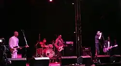 Six hommes caucasiens sur scène, dont un est légèrement écarté