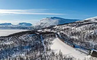 Malmbanan, tiré par une locomotive Bombardier IORE, entre Björkliden et Kopparåsen, un poteau d'arrêt ferroviaire. Vers la gauche la vallée Lapporten. Mars 2023.