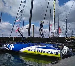 Vu de trois quarts arrière, voilier bleu, blanc et jaune amarré au ponton.