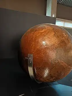 Globe entier brun clair et brun foncé. Il est centré sur le sud où est représentée un large continent.