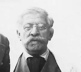 Homme au gros nez avec des lunettes rondes, une moustache volumineuse et des cheveux gris