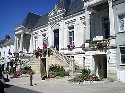 Photographie en couleur d'un bâtiment municipal et de son parvis longés par une voie publique.