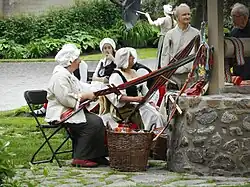 Des artisanes en costume d'époque réalisent des ceintures fléchées à l'extérieur.