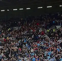 Photo des supporters de Manchester City, en tribune dos tourné au terrain, effectuant la danse du Poznań.