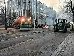 Plusieurs tracteurs dans une rue de Dijon, à l'angle d'un grand bâtiment vitré, dont un déverse des déchets agricoles