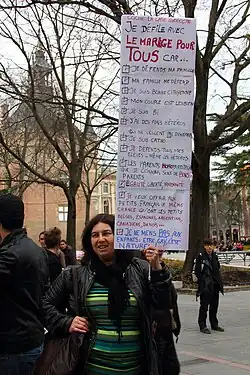 Une femme lors d'une manifestation à Toulouse. Elle tient une pancarte « cocher la case correcte, Je défile pour le mariage pour tous car... » où toutes les propositions sont cochées. Celles-ci sont « Je défend ma famille », « Ma famille me défend », « Je suis bonne citoyenne », « Mon couple est lesbien », « Je suis bi », « J'ai des amis hétéros qui ne veulent pas d'enfant » (le pas est souligné), « Je suis catho », « Je défends tous mes élèves - mêmes les hétéros », « les parents homoparentaux que je connais sont de bons parents » (« homo » et « bons » sont écrits d'une autre couleur), « égalité, liberté, fraternité », « je veux offrir aux petits Français la même chance qu'ont les petits Belges, Espagnols, Argentins, Canadiens, Danois », « je ne mens pas aux enfants, être gay est naturel ! » (« pas » est souligné).
