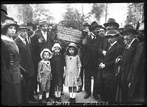 Photographie montrant des hommes, des femmes et de jeunes enfants autour d'une gerbe de fleurs.