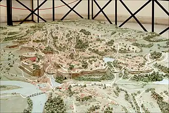 Photographie en couleurs d'une maquette représentant un site de collines près d'un fleuve et quelques bâtiments.