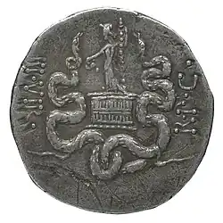 Personnage tenant un bâton et une coupe, debout sur un coffre en osier, encadré de deux serpents.