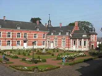 vue sur un jardin carré, derrière lequel s'élève un château rose à un étage, plus un étage sous un toit d'ardoise
