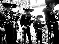 Photographie montrant un groupe de musiciens mexicains vêtus de tenues traditionnelles et coiffés de sombreros.