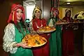 Marocaines en habits traditionnels présentant des plats de couscous.