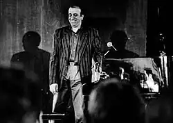 Martial Solal sur scène, souriant debout à côté de son piano en 1998. Il porte une chemise et une veste. On devine les têtes du public au premier plan. La photo est en noir et blanc.