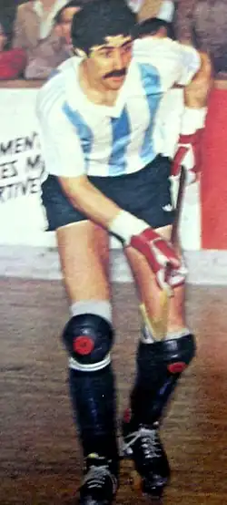  Photographie d'un joueur de rink hockey sur ses patins avec un maillot blanc et bleu