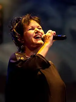 Une femme dans une tenue noire portant un micro dans sa main droite.