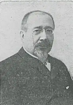 Portrait photographique d'un homme portant une barbiche et de fines lunettes.