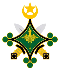 Emblème composé de deux épées noires, dorées et argentées, croisées derrière une étoile à quatre branches verte et noire, qui porte en son centre un caducée doré, sur sa pointe supérieure un croissant et une étoile dorée et sur chaque autres pointe trois pois verts.