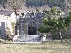 Photographie en couleurs d'un édifice ancien au second plan d'une aire engazonnée.