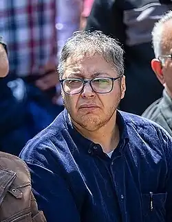 Homme en chemise bleue avec des cheveux gris portant des lunettes et faisant une grimace