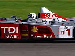 Photographie d'une voiture d'endurance grise et rouge, vue en gros plan, de profil.