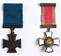Deux médailles militaires de style victorien sur fond blanc : une croix de guerre en bronze foncé avec un lion et une croix blanche ornée d'une couronne, chacune avec des bandes colorées.