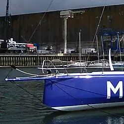 De profil, avant d'un voilier bleu. L'étrave est légèrement spatulée.