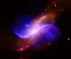 Image composite de M106 utilisant les données captées dans le visible par le relevé DSS (en jaune), dans le domaine des ondes radio par le VLA (en violet), dans le domaine des rayons X par le télescope spatial Chandra (en bleu) et dans l'infrarouge par le télescope spatial Spitzer (en rouge).