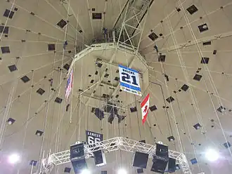 Photo de la bannière dédiée à Michel Briere au milieu de câbles tombant du plafond de la Mellon Arena; on distingue également les drapeaux américains, canadiens et la bannière dédiée à Mario Lemieux.