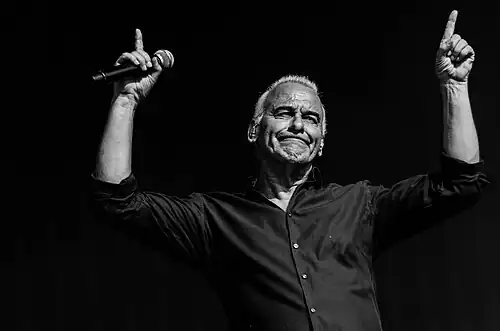 Photo en noir et blanc d'un homme levant les doigts en l'air avec un micro dans la main droite.
