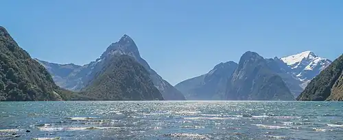 L'eau de l'océan au premier plan, et au fond des montagnes très découpées.