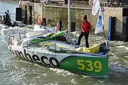 À l'arrière, tête du skipper émergeant derrière la grand-voile affalée. À l'avant, une femme debout.