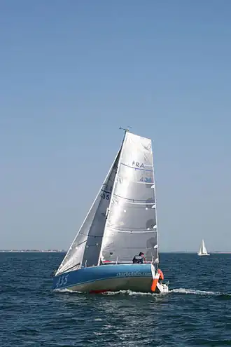 Petit voilier bleu en mer, progressant sous voile argentée.