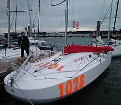 Bateau blanc à l'avant très large et très arrondi, amarré au ponton. Il porte en rouge le numéro 1028.