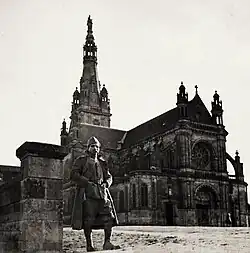 Photographie en noir et blanc d'un homme debout, vêtu d'un uniforme militaire, posant devant une église.