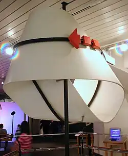 Photo d’une œuvre. Un ruban blanc torsadé agrémenté d’une flèche rouge.