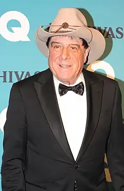 Photo d'un homme blanc dans la soixantaine portant un smoking noir avec un nœud papillon de la même couleur et un grand chapeau de cowboy brun clair.