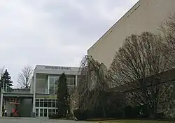 Une entrée de bâtiment à gauche et des arbres devant un mur.