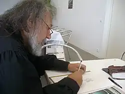 La photo montre un homme barbu assis de profil.