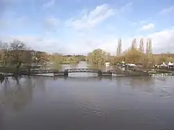 photographie en couleurs d'un cours d'eau dont le niveau attend la base d'une passerelle et qui noie les rives.