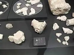 Photo de multiples bouts de pierre blanche sur un plan d'exposition gris très sombre.