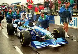 Photo d'une monoplace bleue et blanche, entourée de plusieurs personnes