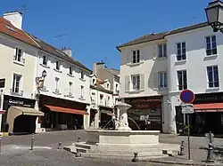 Fontaine en pierre blanche, à quatre jets, devant des immeubles anciens à façade blanche