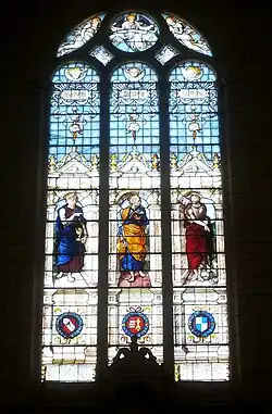 Vue, depuis l'intérieur, de la verrière d'une église représentant trois saint catholiques.