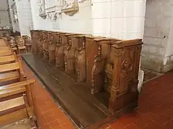 Vue de sept stalles en bois alignées contre le mur intérieur d'une église.