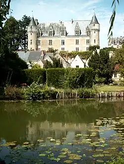 Vue d'un château sur une hauteur avec des maisons en contrebas et un cours d'eau au premier plan.