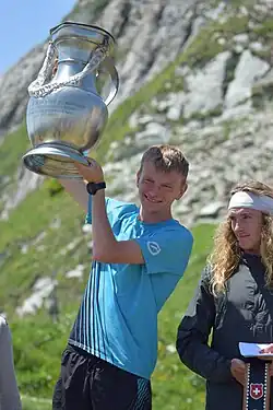 Homme blond souriant soulevant une channe géante en étain.