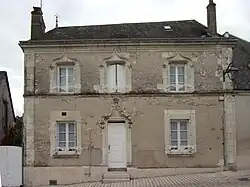 Photographie en couleurs d'une maison à étage dont le tympan de la porte d'entrée et le linteau des fenêtres est ouvragé.