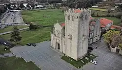 Église ancienne en appareil régulier à proximité d'un vaste parc de stationnement automobile.