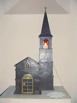 Tabernacle en fer embouti dans l'église Saint-Hilaire de Moulin-Mage dans le Tarn (dont il reproduit le clocher et le porche), avec la veilleuse allumée.